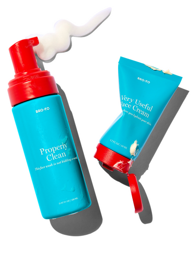 Two blue skincare products with red lids are shown: a foaming face wash dispensing white foam on the left, and a slightly squeezed cream tube on the right. Both cast shadows on a white background.