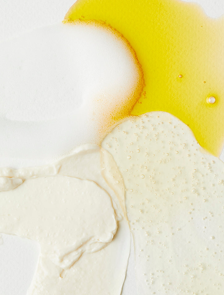 Abstract composition of skincare or beauty product textures in white, cream, and yellow tones, featuring foamy, creamy, and oily substances with bubbles on a white background.