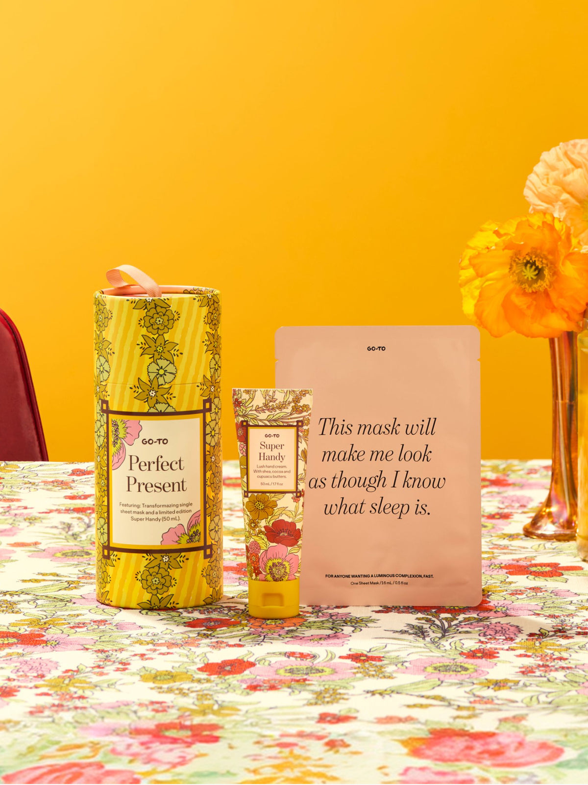 Go-To Skincare Perfect Present gift set with a floral yellow box plus Super Handy hand cream and Transformazing sheet mask on a colorful floral table