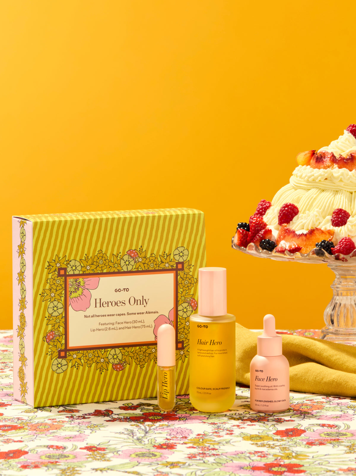 Go To Skincare Heroes Only gift set with a floral yellow box and three skincare bottles styled beside a celebratory layered cake on a colorful tablecloth