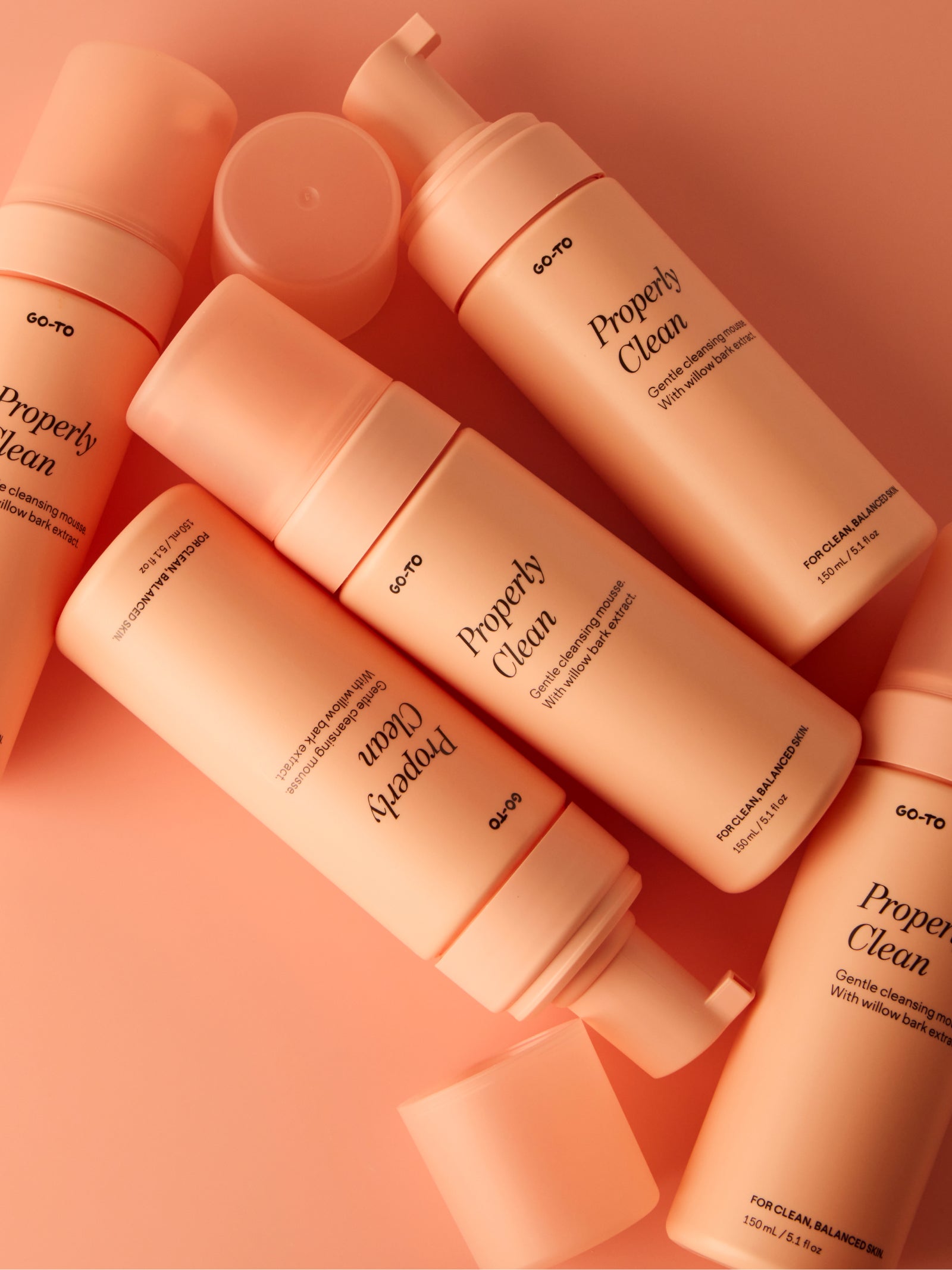 Peach-colored bottles of "Properly Clean" cleansing mousse with willow bark extract, arranged on a matching background.