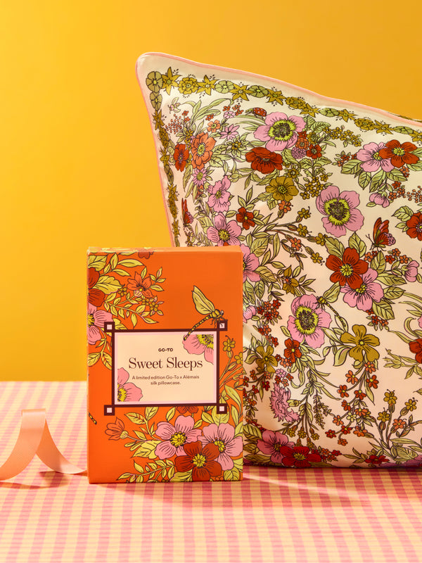 Floral Sweet Sleeps silk pillowcase and matching gift box displayed on a pink checkered surface against a bright orange background from Go To Skincare